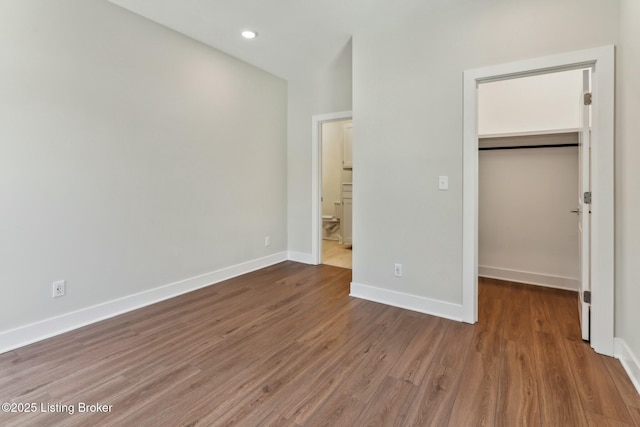 unfurnished bedroom with recessed lighting, baseboards, wood finished floors, and a spacious closet