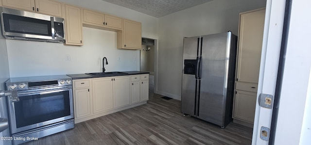 kitchen featuring a textured ceiling, dark wood-type flooring, a sink, appliances with stainless steel finishes, and dark countertops