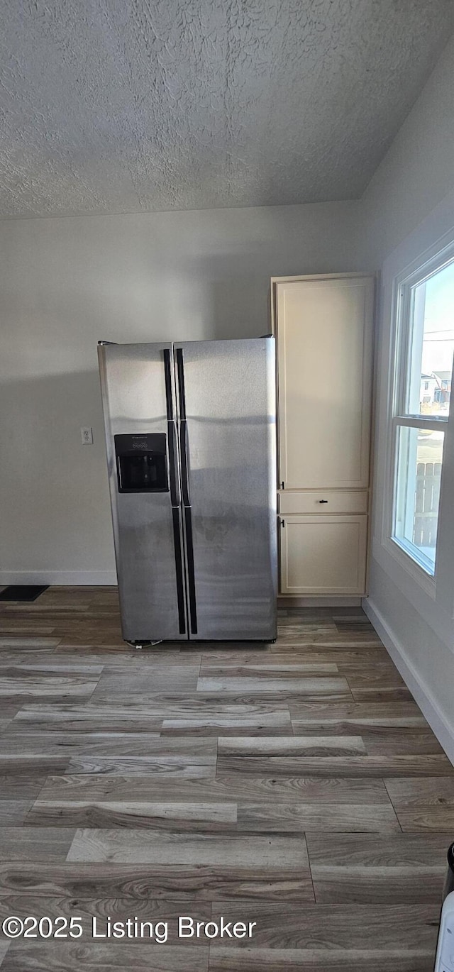 kitchen featuring light wood finished floors, baseboards, stainless steel refrigerator with ice dispenser, and a textured ceiling