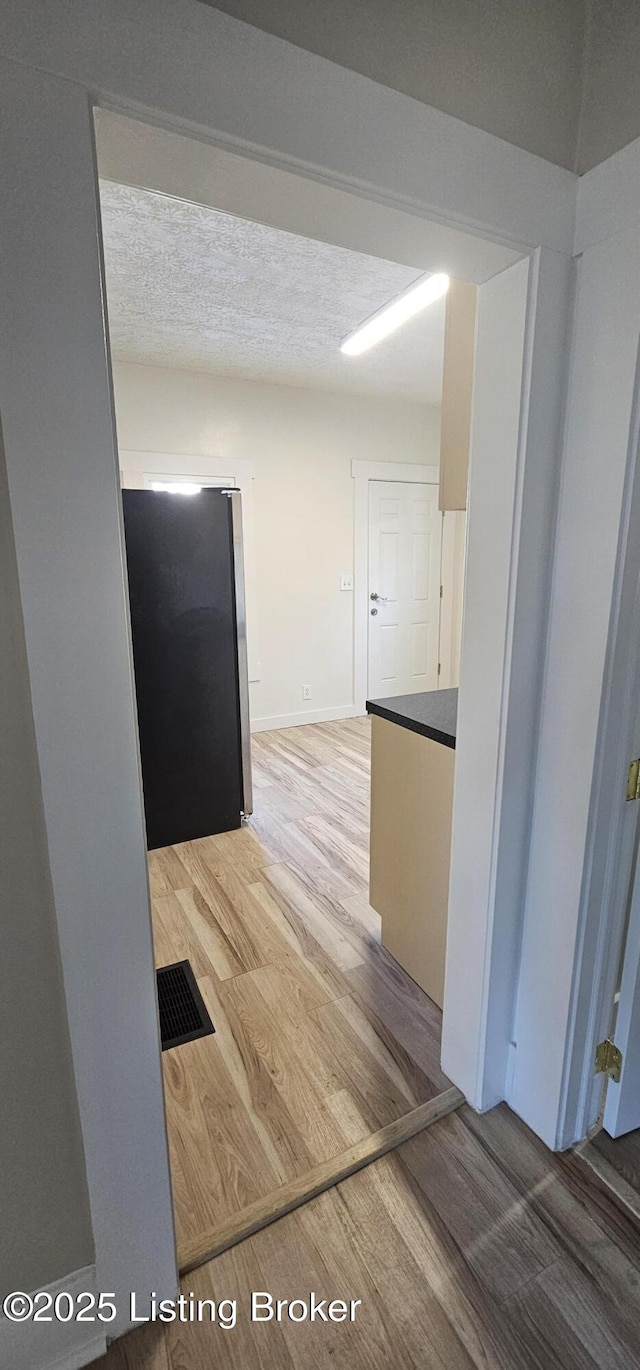 corridor with a textured ceiling, visible vents, and wood finished floors