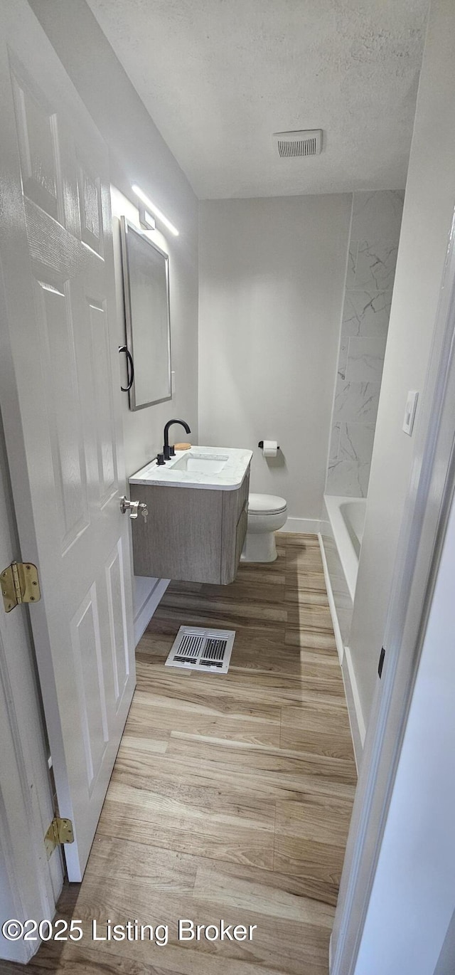 full bathroom featuring visible vents, toilet, vanity, a textured ceiling, and wood finished floors