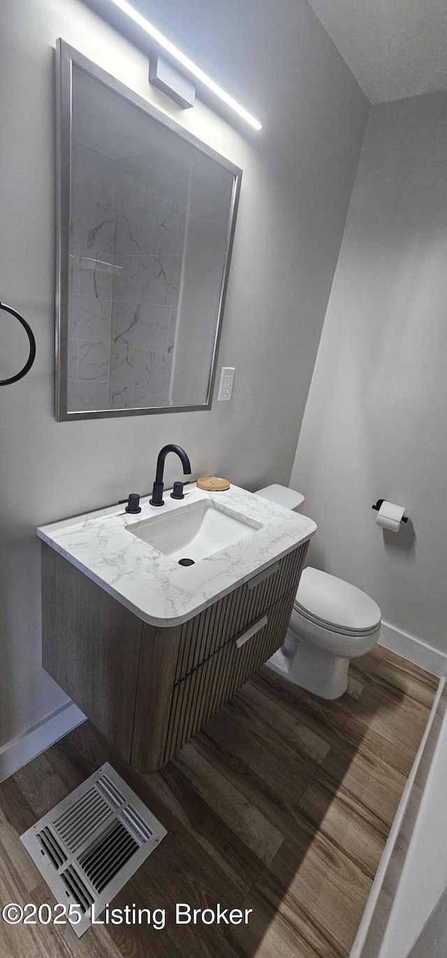 half bathroom with toilet, wood finished floors, visible vents, a sink, and baseboards