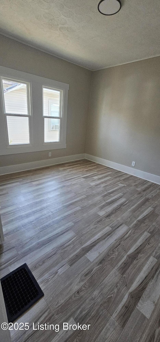 empty room with visible vents, a textured ceiling, baseboards, and wood finished floors