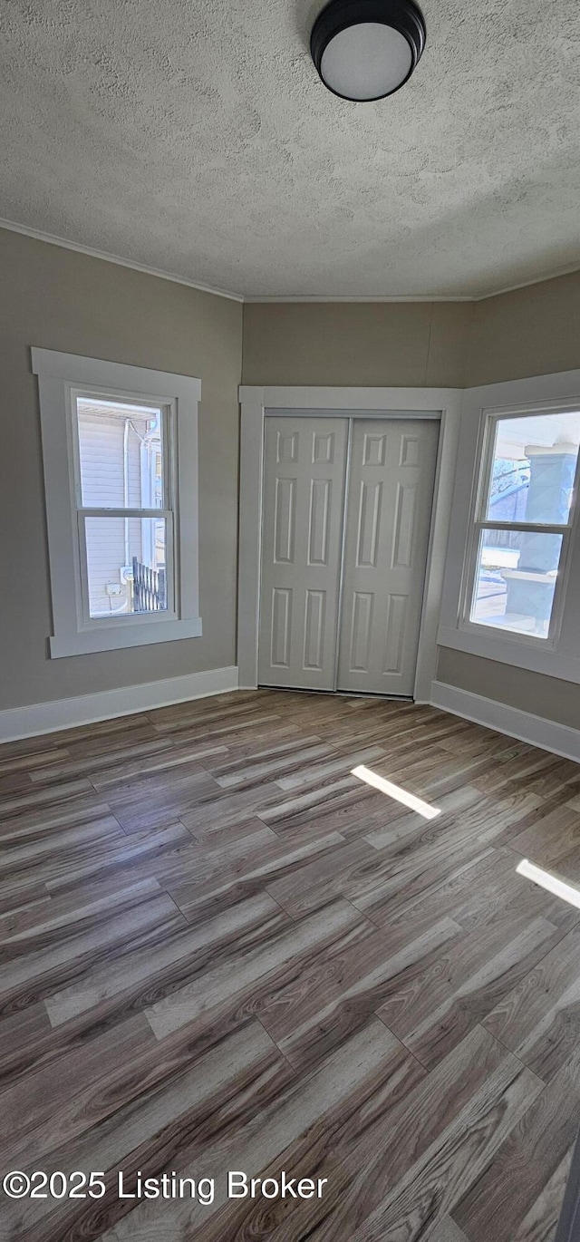 unfurnished bedroom with a closet, multiple windows, baseboards, and wood finished floors