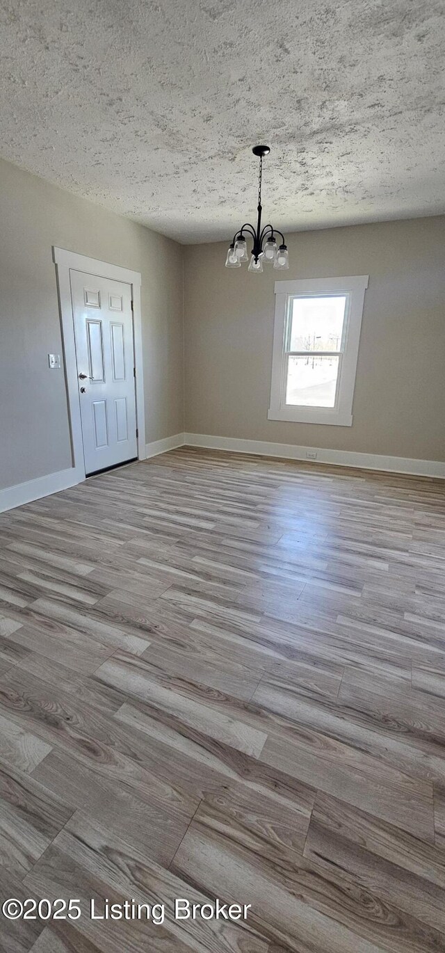 unfurnished dining area featuring a textured ceiling, light wood-type flooring, a notable chandelier, and baseboards