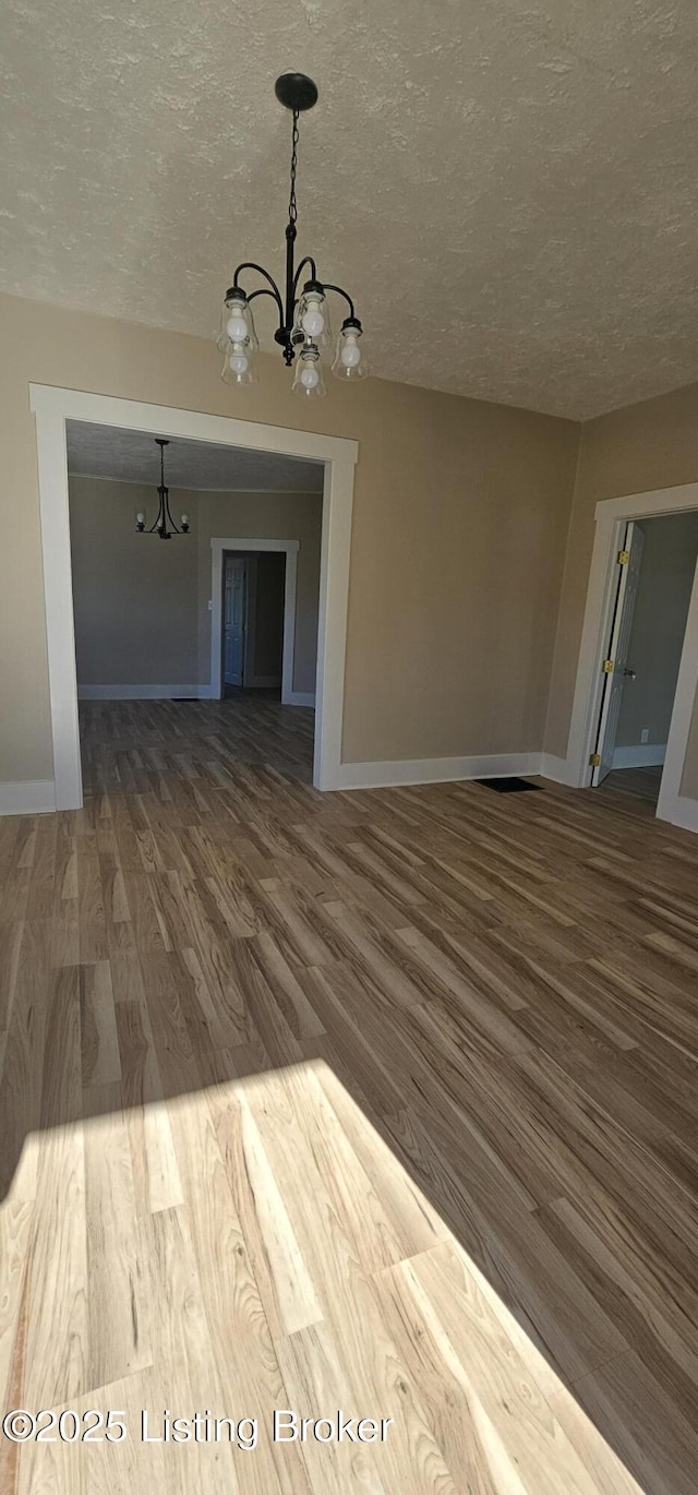 unfurnished dining area with a chandelier, a textured ceiling, baseboards, and wood finished floors