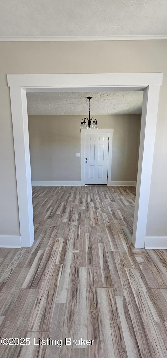 spare room with a chandelier, light wood-style flooring, baseboards, and a textured ceiling