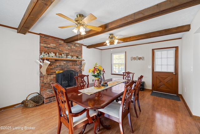 dining area with a textured ceiling, a brick fireplace, hardwood / wood-style flooring, and beamed ceiling