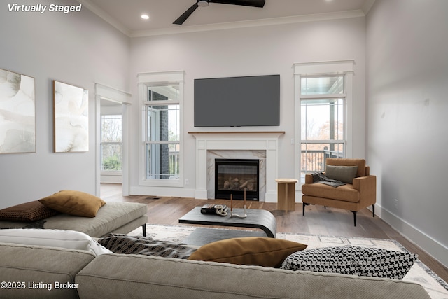 living room with crown molding, ceiling fan, wood-type flooring, and a high end fireplace