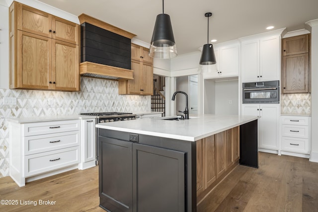 kitchen with pendant lighting, white cabinetry, sink, oven, and a kitchen island with sink