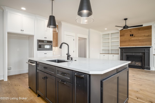 kitchen featuring sink, a kitchen island with sink, wall oven, light stone counters, and white cabinets