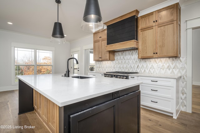 kitchen featuring sink, white cabinets, hanging light fixtures, a kitchen island with sink, and custom range hood