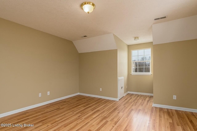 additional living space with a textured ceiling, light hardwood / wood-style flooring, and lofted ceiling