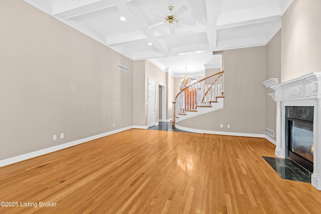 unfurnished living room with ceiling fan with notable chandelier, a high end fireplace, light hardwood / wood-style floors, beam ceiling, and coffered ceiling