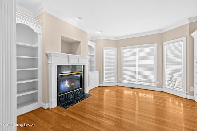 unfurnished living room with hardwood / wood-style flooring, built in features, crown molding, and a fireplace