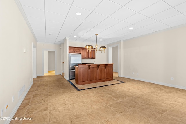 kitchen with a kitchen island, pendant lighting, ornamental molding, stainless steel fridge, and a chandelier