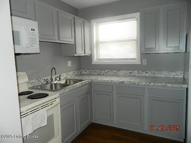 kitchen with light stone countertops, sink, gray cabinetry, and white appliances