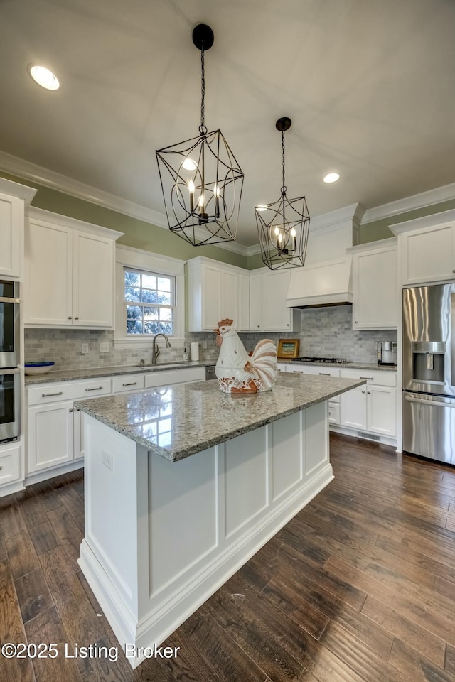 kitchen featuring stainless steel appliances, a sink, ornamental molding, a center island, and dark wood-style floors