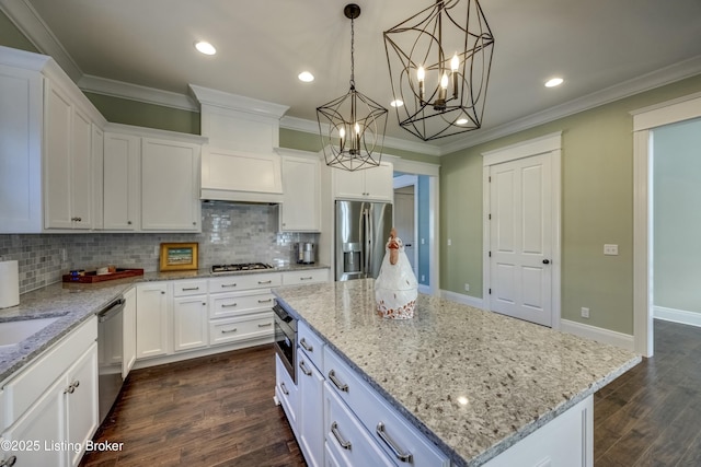 kitchen with dark wood finished floors, a kitchen island, appliances with stainless steel finishes, ornamental molding, and white cabinetry