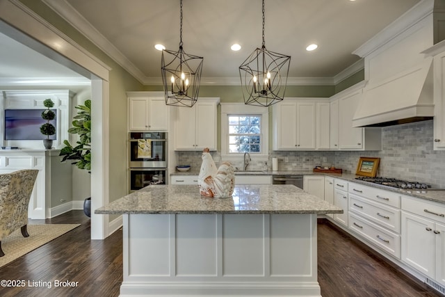 kitchen featuring crown molding, stainless steel appliances, white cabinets, a sink, and a kitchen island