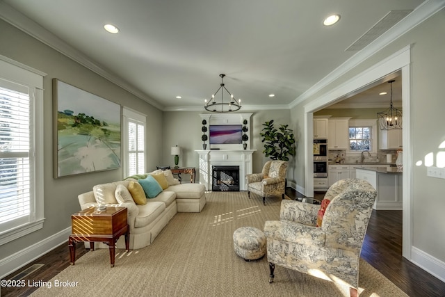 living room with dark wood-style floors, crown molding, a fireplace, and an inviting chandelier