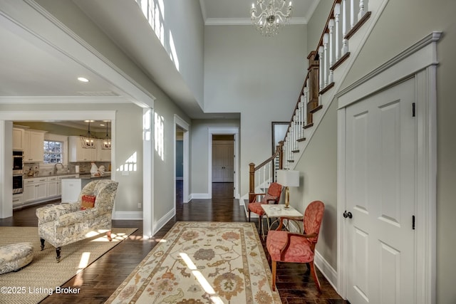 entrance foyer with crown molding, stairway, dark wood-type flooring, and a notable chandelier