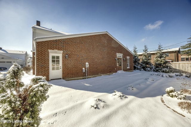 snow covered back of property with brick siding and a chimney