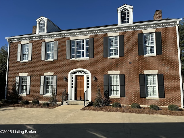 colonial inspired home featuring a chimney and brick siding