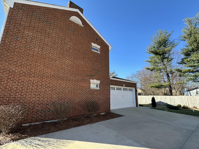 view of side of property with a garage, concrete driveway, brick siding, and fence