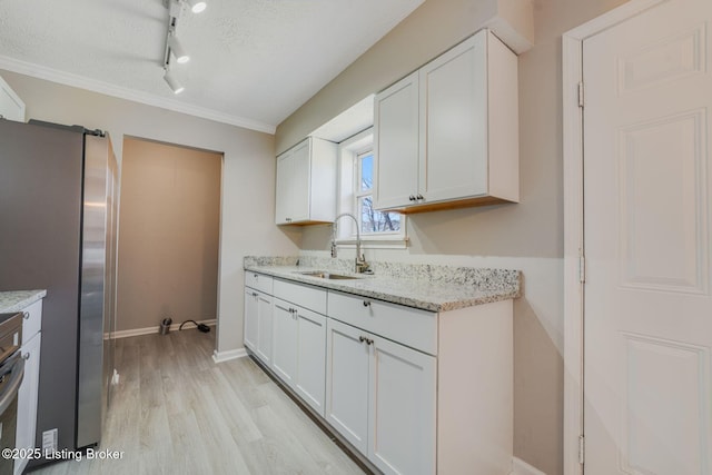 kitchen featuring white cabinetry, light stone countertops, sink, and stainless steel refrigerator