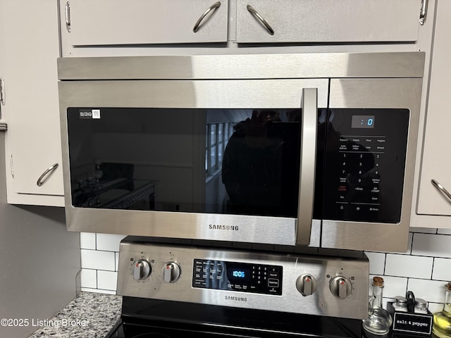 interior details with tasteful backsplash, white cabinetry, stainless steel appliances, and light stone counters