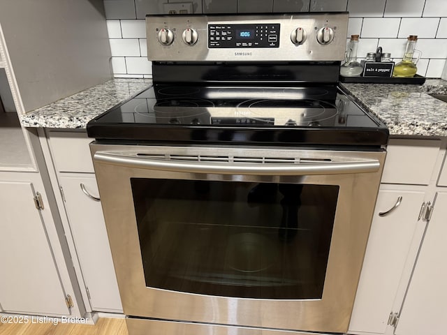 details with light stone counters, decorative backsplash, stainless steel range with electric cooktop, and white cabinets