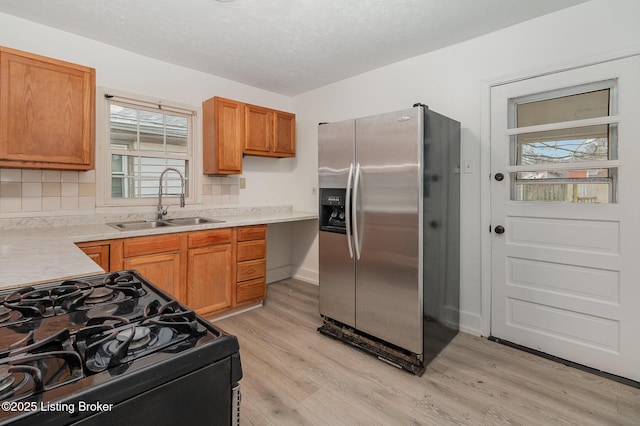 kitchen with sink, stainless steel fridge, light hardwood / wood-style floors, and black gas range