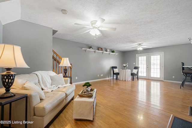 living room with a textured ceiling, ceiling fan, light hardwood / wood-style floors, and french doors