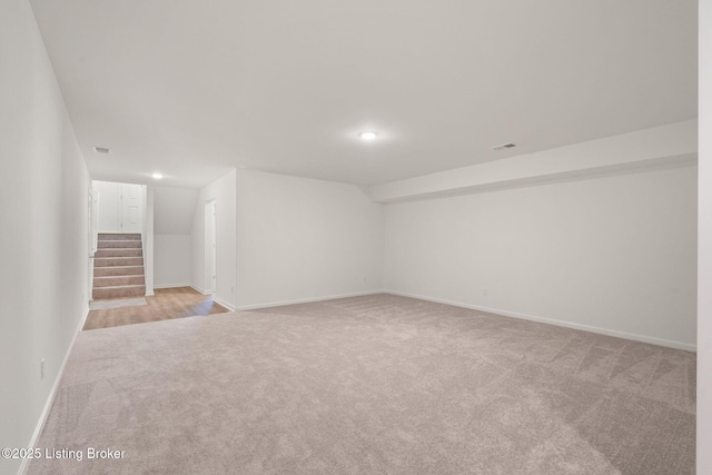 finished below grade area featuring light colored carpet, baseboards, and stairs