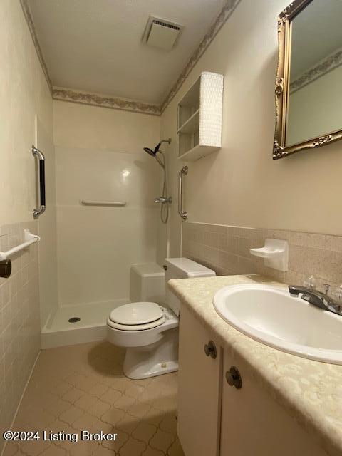 bathroom featuring toilet, tile patterned flooring, tile walls, walk in shower, and vanity