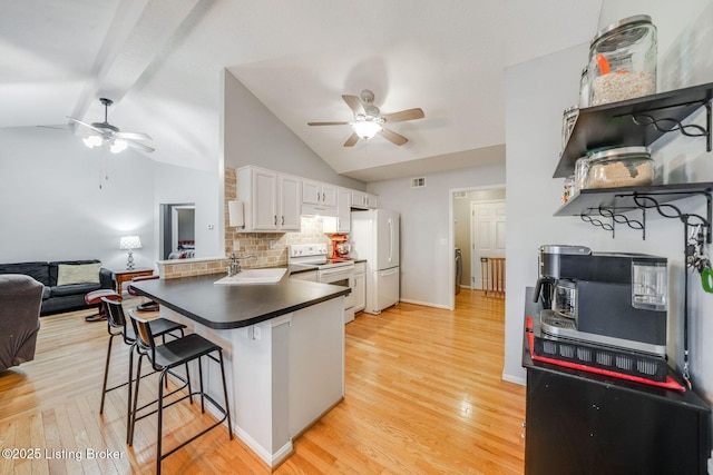 kitchen with white appliances, white cabinets, kitchen peninsula, a breakfast bar, and backsplash