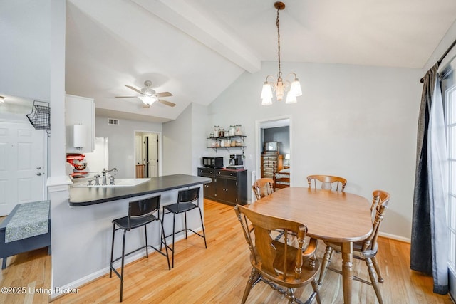 dining room featuring ceiling fan, sink, light hardwood / wood-style flooring, and vaulted ceiling with beams