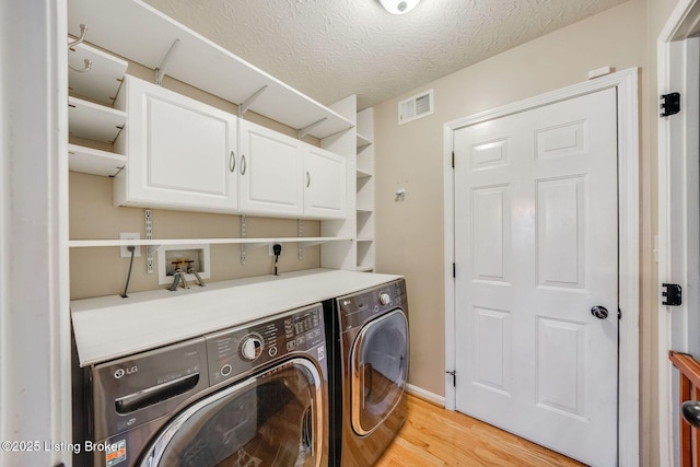 laundry room featuring cabinets, a textured ceiling, separate washer and dryer, and light hardwood / wood-style floors