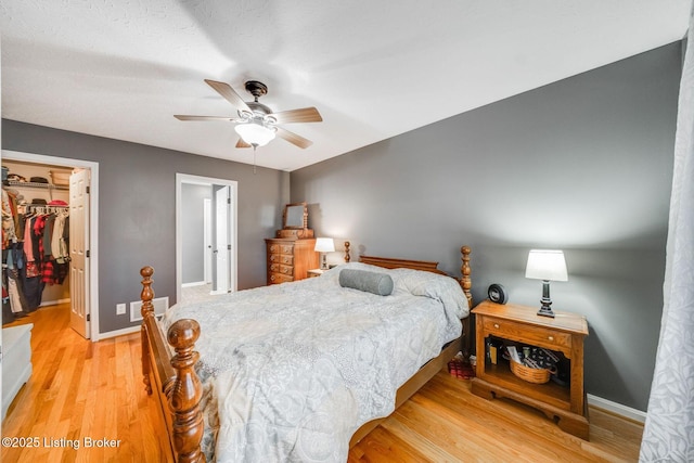 bedroom with ceiling fan, light wood-type flooring, a closet, and a spacious closet