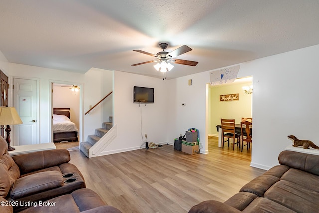 living room featuring light wood-type flooring, ceiling fan, and a textured ceiling