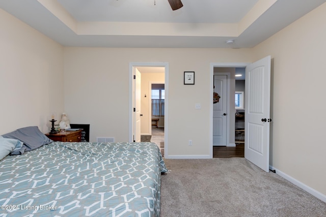 bedroom featuring ceiling fan, light colored carpet, and a tray ceiling