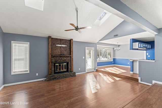 unfurnished living room with ceiling fan with notable chandelier, a skylight, a fireplace, high vaulted ceiling, and hardwood / wood-style flooring