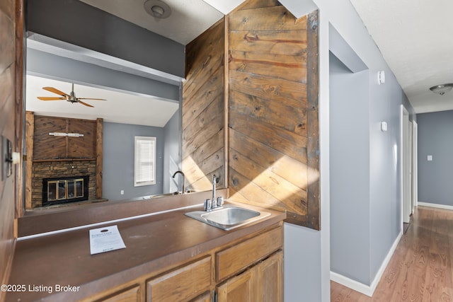 kitchen featuring ceiling fan, vaulted ceiling with beams, sink, light wood-type flooring, and a stone fireplace