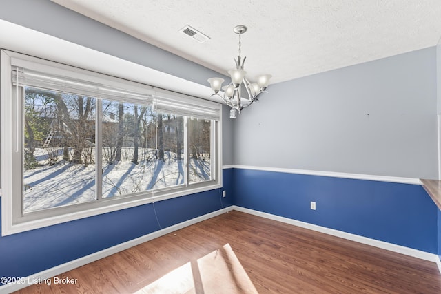 unfurnished dining area with a healthy amount of sunlight, a textured ceiling, a chandelier, and hardwood / wood-style floors