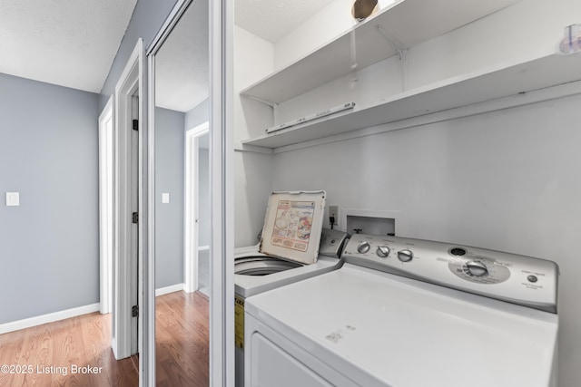 clothes washing area featuring a textured ceiling, washing machine and dryer, and light wood-type flooring