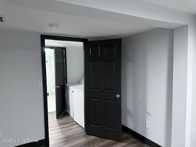 hallway featuring washing machine and dryer, visible vents, baseboards, and wood finished floors