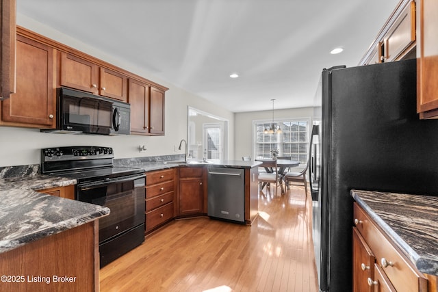 kitchen with black appliances, dark stone counters, hanging light fixtures, light hardwood / wood-style floors, and kitchen peninsula