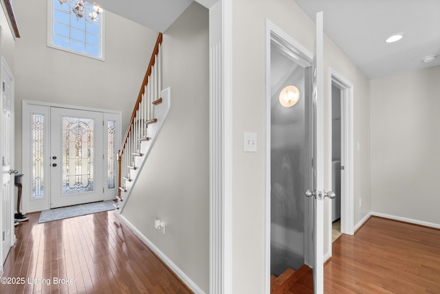 foyer entrance with hardwood / wood-style flooring, a towering ceiling, and a chandelier