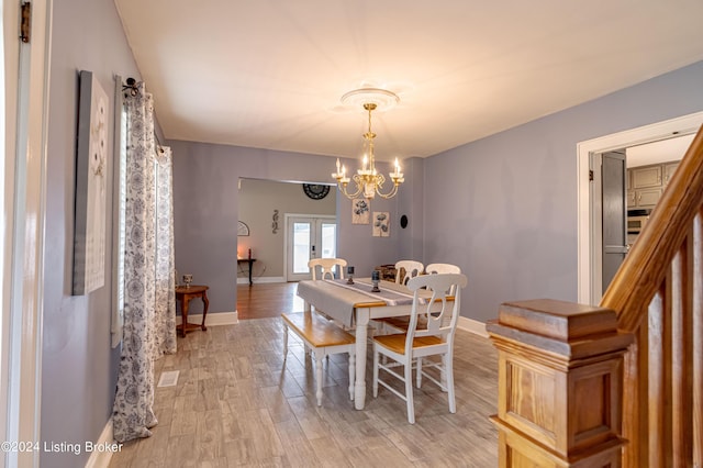 dining area featuring light wood-type flooring, french doors, and a notable chandelier